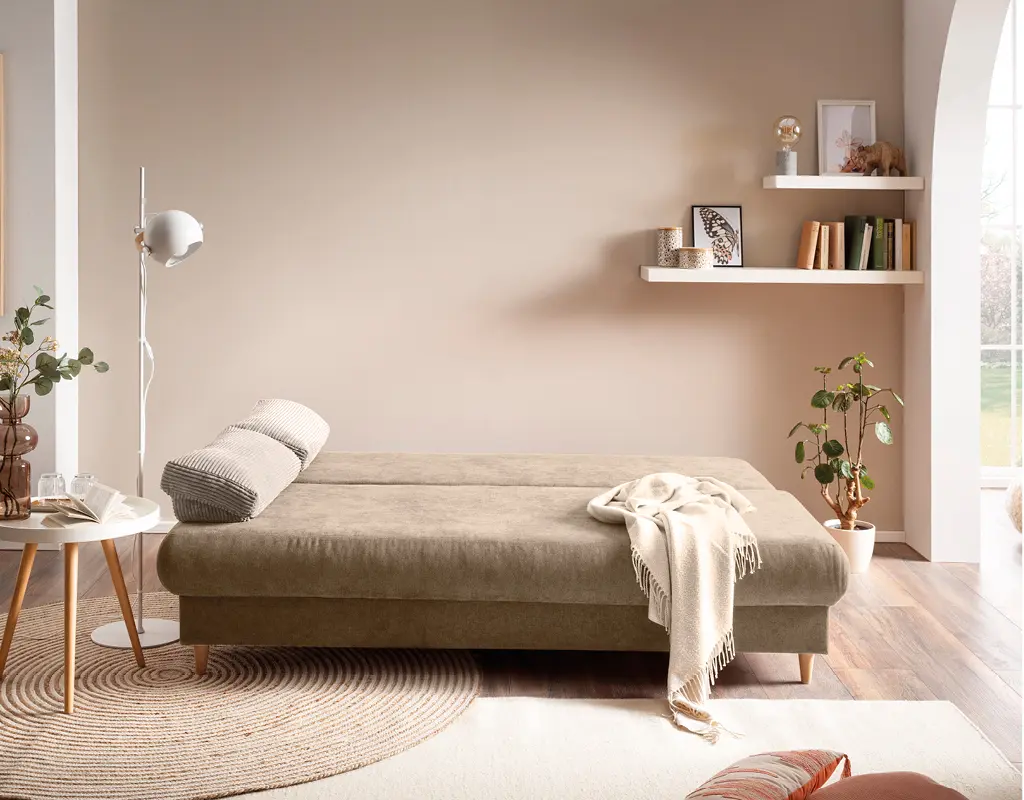 Beiges Schlafsofa in gemütlichem Raum mit Deko und Pflanzen. Multifunktionales Gästebett mit weicher Liegefläche und wohnlicher Einrichtung für entspanntes Wohnen.